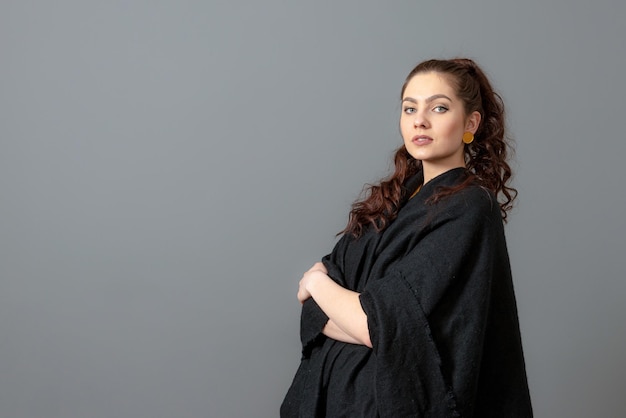 portrait of charming curlyhaired teenager woman in a black cloak isolated on a gray background