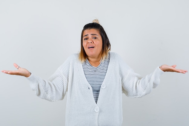 Portrait of charming lady showing helpless gesture in t-shirt, cardigan and looking confused