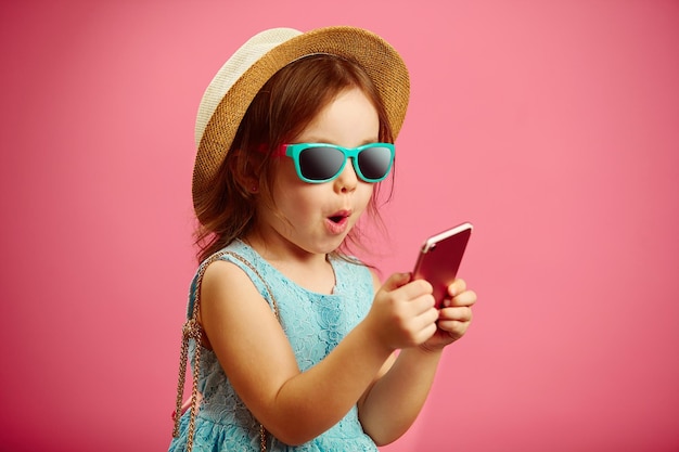 Portrait of charming little girl looking at the phone and sincerely expresses surprise emotion