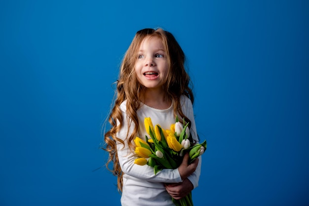 Portrait of a charming smiling little girl with a bouquet of tulips in her hands lifestyle