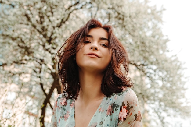 Portrait of charming woman posing near apple cherry tree blossoms blooming flowers in the garden