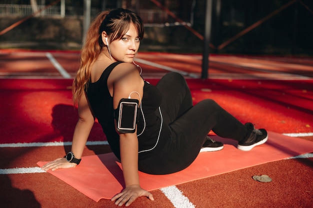 Portrait of a charming young body positive woman looking at camera while sitting on the ground resting after weight loss exercises in the morning.