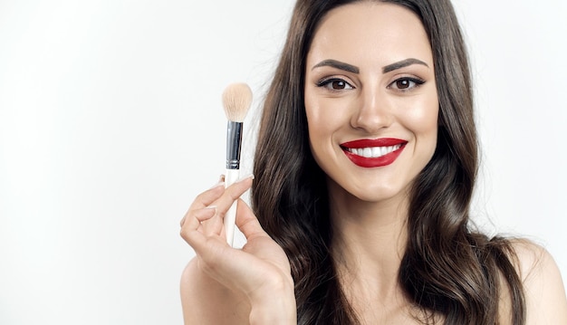 Portrait of charming young woman with brown wavy hair and naked shoulders holding a makeup brush isolated white background copyspace