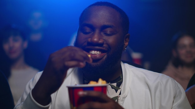 Portrait of cheerful afro american man watching comedy in cinema Joyful african american guy eating popcorn in movie house Closeup happy afro male person laughing in movie theater