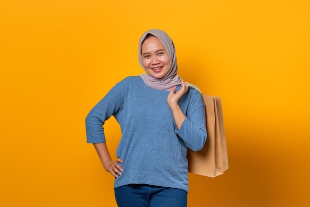 Portrait of cheerful Asian woman holding shopping bag over yellow background