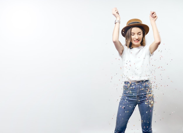 Portrait of a cheerful beautiful girl wearing hat standing under confetti rain and celebrating isolated over white background hight quality