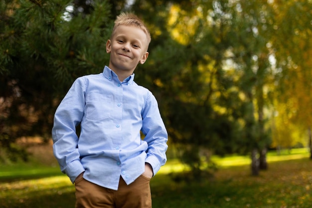 Portrait of a cheerful boy in a blue shirt standing with his hands in his pockets against the