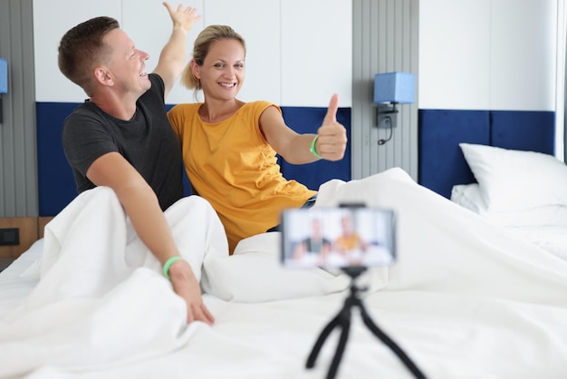 Portrait of cheerful couple making photos in hotel room in bad smiling woman showing thumb up