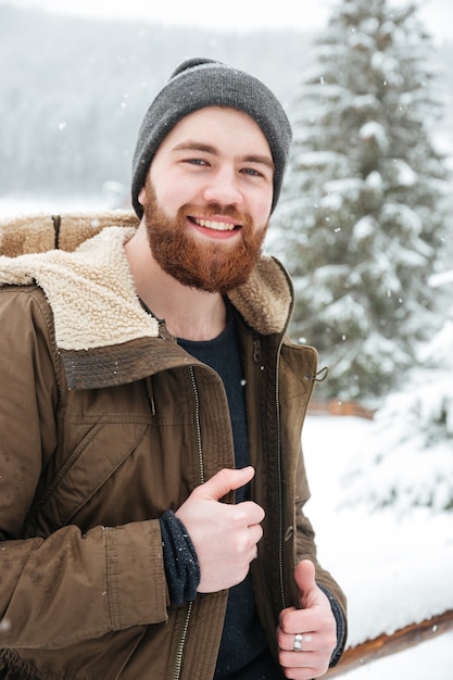 Portrait of cheerful handsome bearded young man standing in winter forest