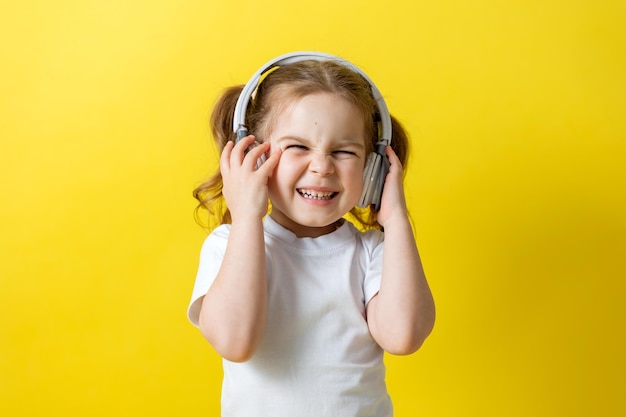 Portrait of a cheerful little girl listening to music with white headphones audiobooks audio lessons