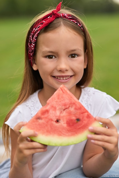 Portrait of cheerful little girl looking at camera while holding watermelon slice family having a