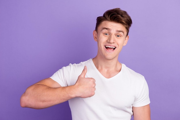 Portrait of cheerful man in basic clothing smiling showing thumbs up at camera isolated over bright background