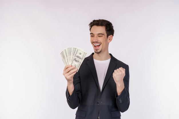 Portrait of a cheerful man holding dollar bills and doing winner gesture clenching fist over white background