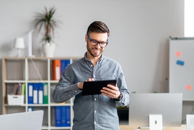 Portrait of cheerful mature businessman using computer tablet in office looking at screen and