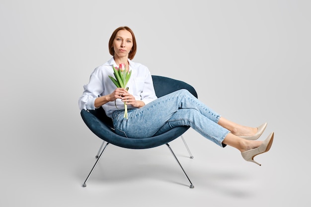 Portrait of cheerful meddle aged woman in armchair with tulips in hand