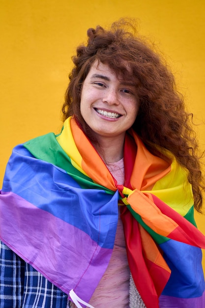 Portrait of cheerful nonbinary person red hair with rainbow flag over shoulders smiling at camera