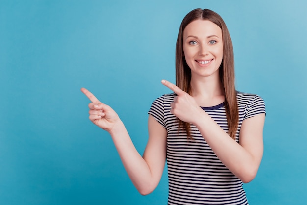 Portrait of cheerful positive girl indicate forefinger empty space toothy smile on blue background