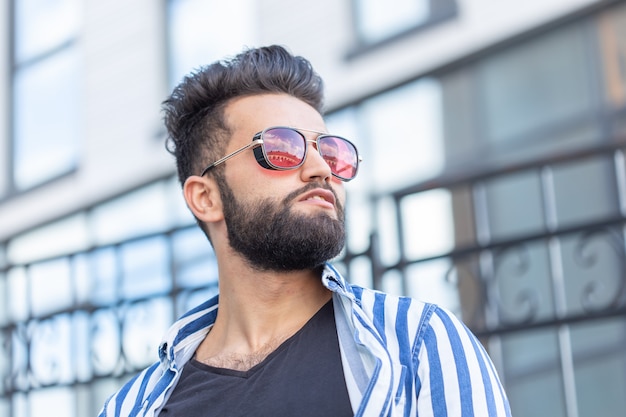 Portrait of cheerful positive stylish student guy in glasses with a mustache and beard outdoors. The concept of successful cheerful people.