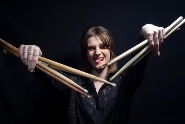 Portrait of a cheerful rock n roll drumming girl holding sticks in her hands Musician in black On a dark background