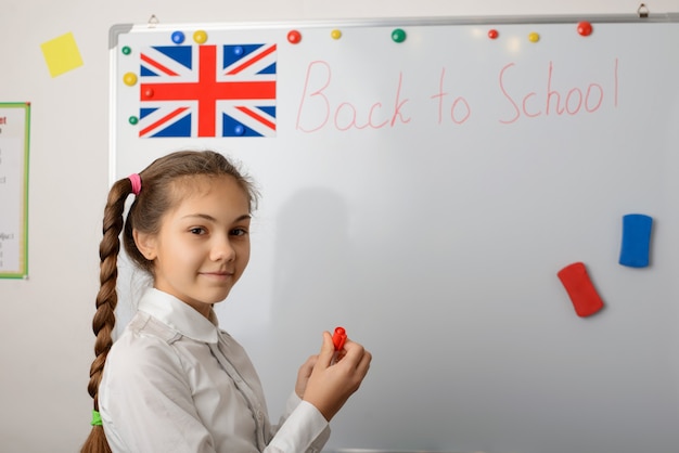 Portrait of a cheerful schoolgirl writing Back to school description on the board