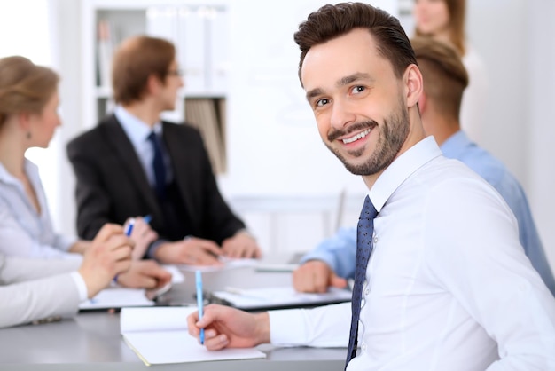 Portrait of cheerful smiling business man  against a group of business people at a meeting.