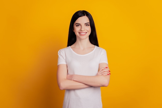 Portrait of a cheerful smiling woman in t-shirt standing with arms folded isolated on the yellow background