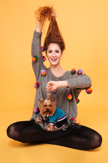 Photo portrait of a cheerful smiling woman with red hair having fun with her dog isolated on orange wall