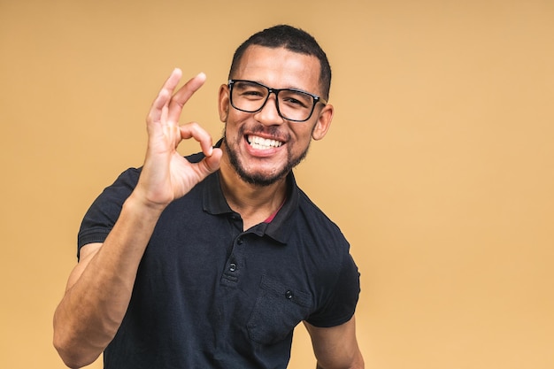 Portrait of a cheerful smiling young african american black man standing isolated over beige background Ok sign