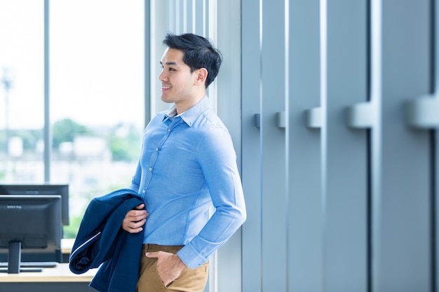 Portrait of a cheerful successful feeling winner handsome young asian businessman wear a business suit of man in blue jacket and blue shirt at window In the office room background