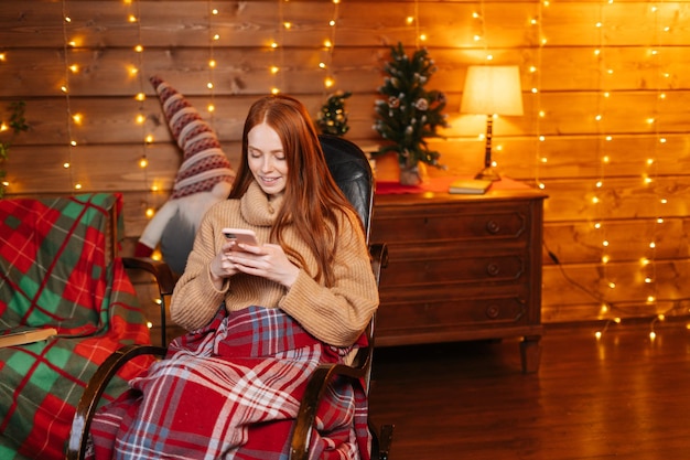 Portrait of cheerful woman typing online message on mobile phone sitting at rocking armchair