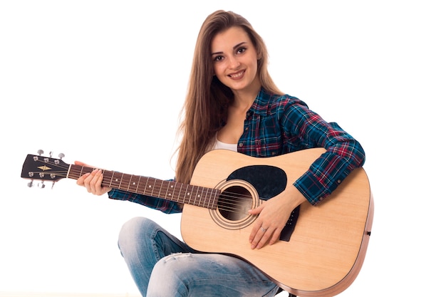 Portrait of cheerful woman with guitar in hands smiling isolated on white wall