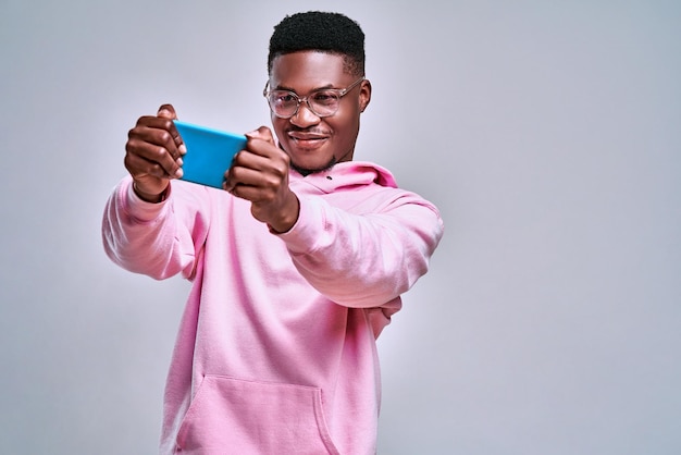 Portrait of cheerful young african man dressed pink hoodie playing games on mobile phone Copy space