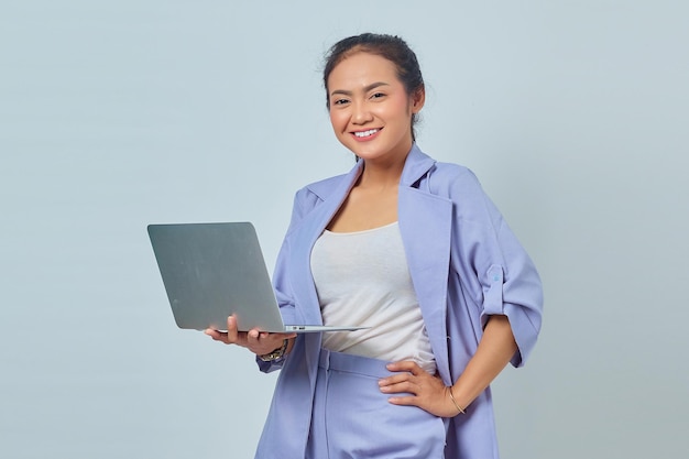 Portrait of cheerful young Asian woman using laptop and looking at camera isolated on white background