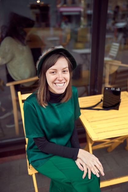 Portrait of cheerful young caucasian woman in green clothes that sitting outside cafe