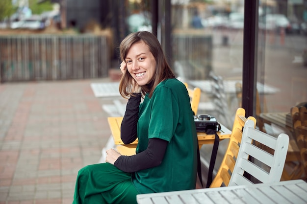 Portrait of cheerful young caucasian woman in green clothes that sitting outside cafe