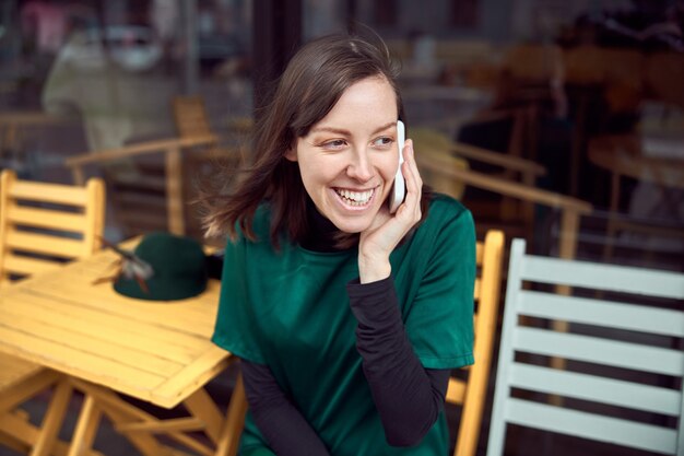 Portrait of cheerful young caucasian woman in green clothes that sitting outside cafe