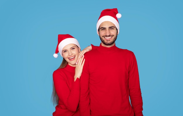 Photo portrait of cheerful young couple in santa hats posing over blue background