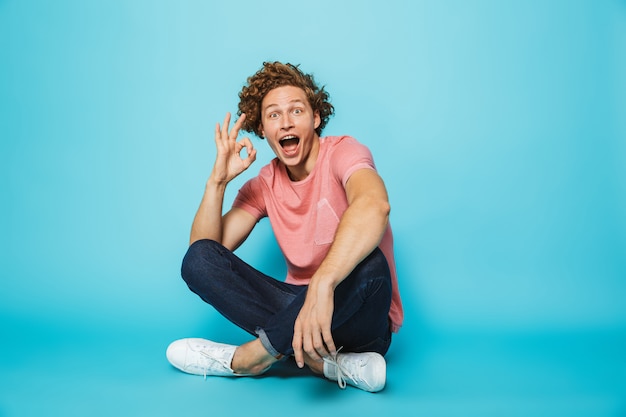 Portrait of a cheerful young curly haired man showing ok