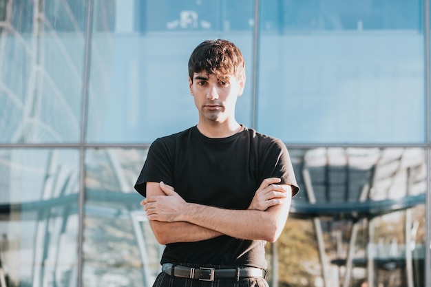 Portrait of cheerful young man in casual with crossed arms serious outdoors in front of a office building in city outdoors. Copy space