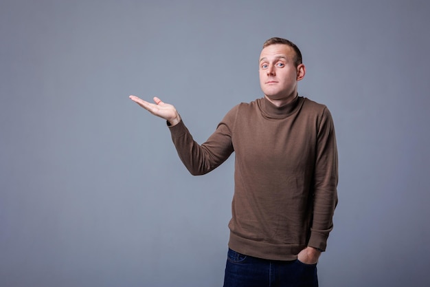 Portrait of cheerful young man smiling while looking at camera pointing with finger on gray background