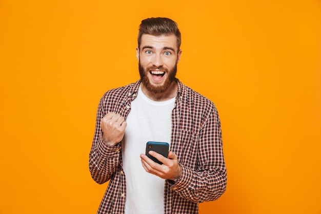 Portrait of a cheerful young man wearing casual clothes using mobile phone