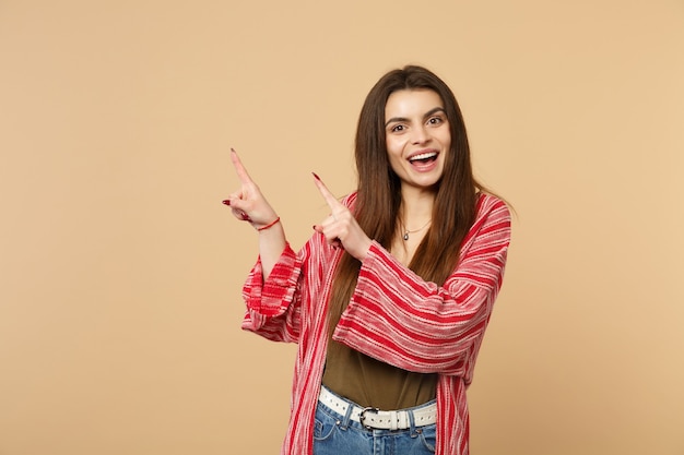 Portrait of cheerful young woman in casual clothes looking camera pointing index fingers aside isolated on pastel beige wall background. People sincere emotions, lifestyle concept. Mock up copy space.