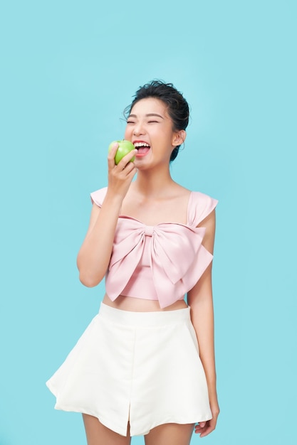 Portrait of a cheerful young woman eating green apple isolated over blue background