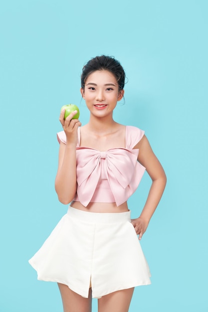 Portrait of a cheerful young woman eating green apple isolated over blue background