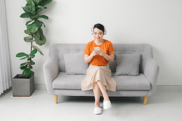 Portrait of a cheerful young woman listening to music with mobile phone while resting on a couch at home