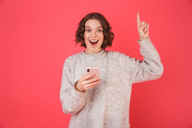 Portrait of a cheerful young woman standing isolated over pink, pointing finger up