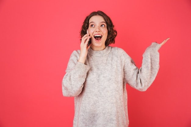 Portrait of a cheerful young woman standing isolated over pink, speaking on mobile phone