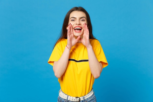 Portrait of cheerful young woman in vivid casual clothes looking camera screaming with hand gesture near mouth isolated on blue background wall in studio. People lifestyle concept. Mock up copy space.