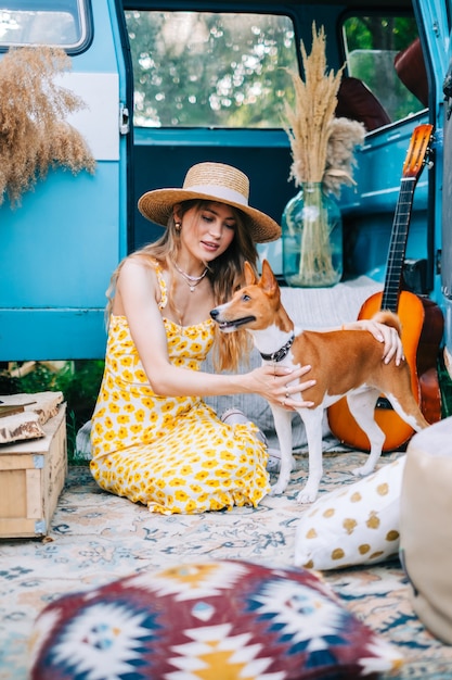 Portrait of cheerful young woman with her dog outdoors near van, simmer traveling concept.