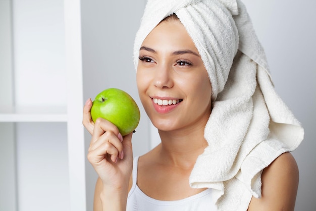 Portrait of a cheerful young woman with perfect smile eating green apple.